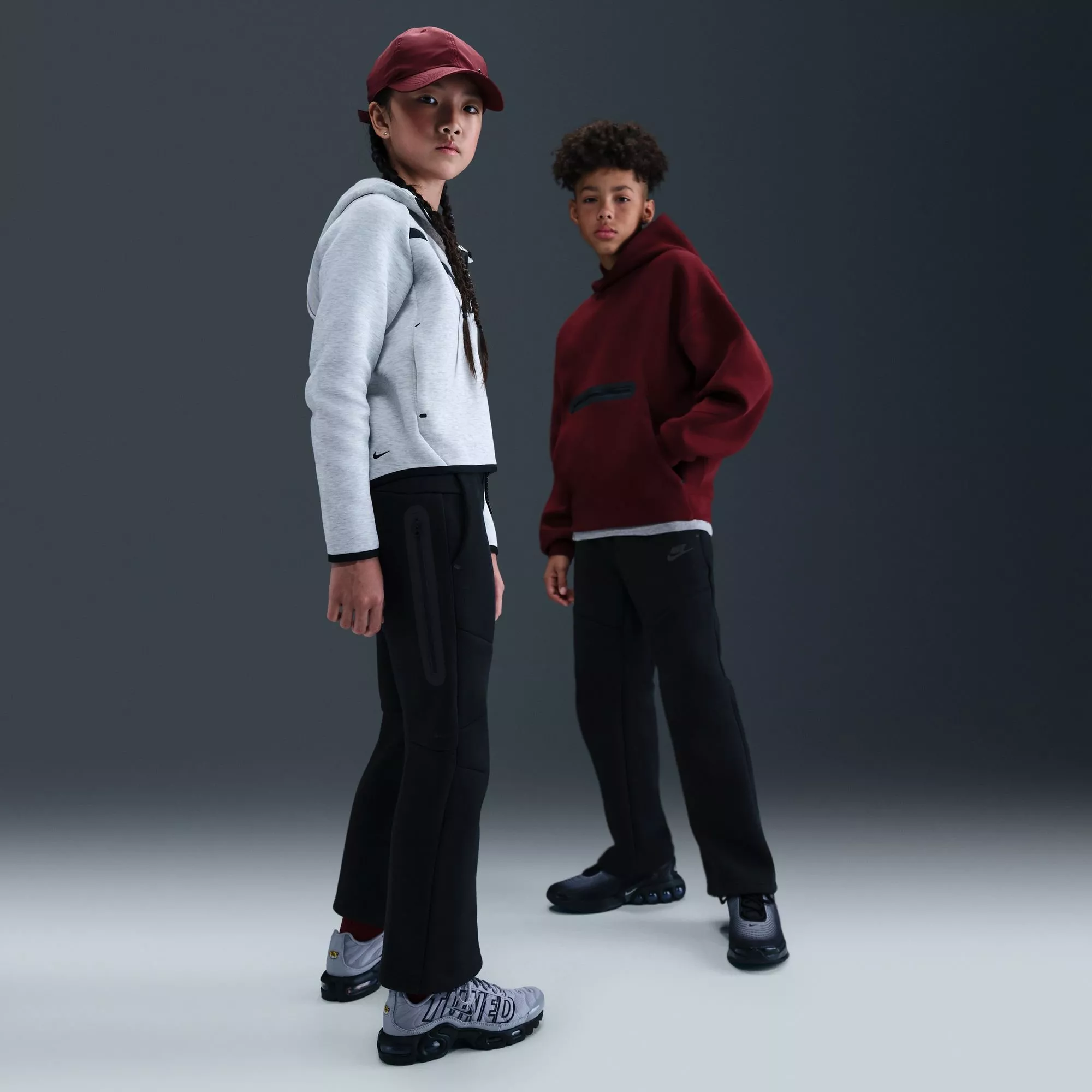 Two children modelling sportswear tracksuits and trainers in a studio, grey hoodie and burgundy hoodie outfit