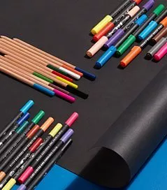 Assorted colourful marker pens and pencils on black paper sheet, art supplies flat lay on desk background