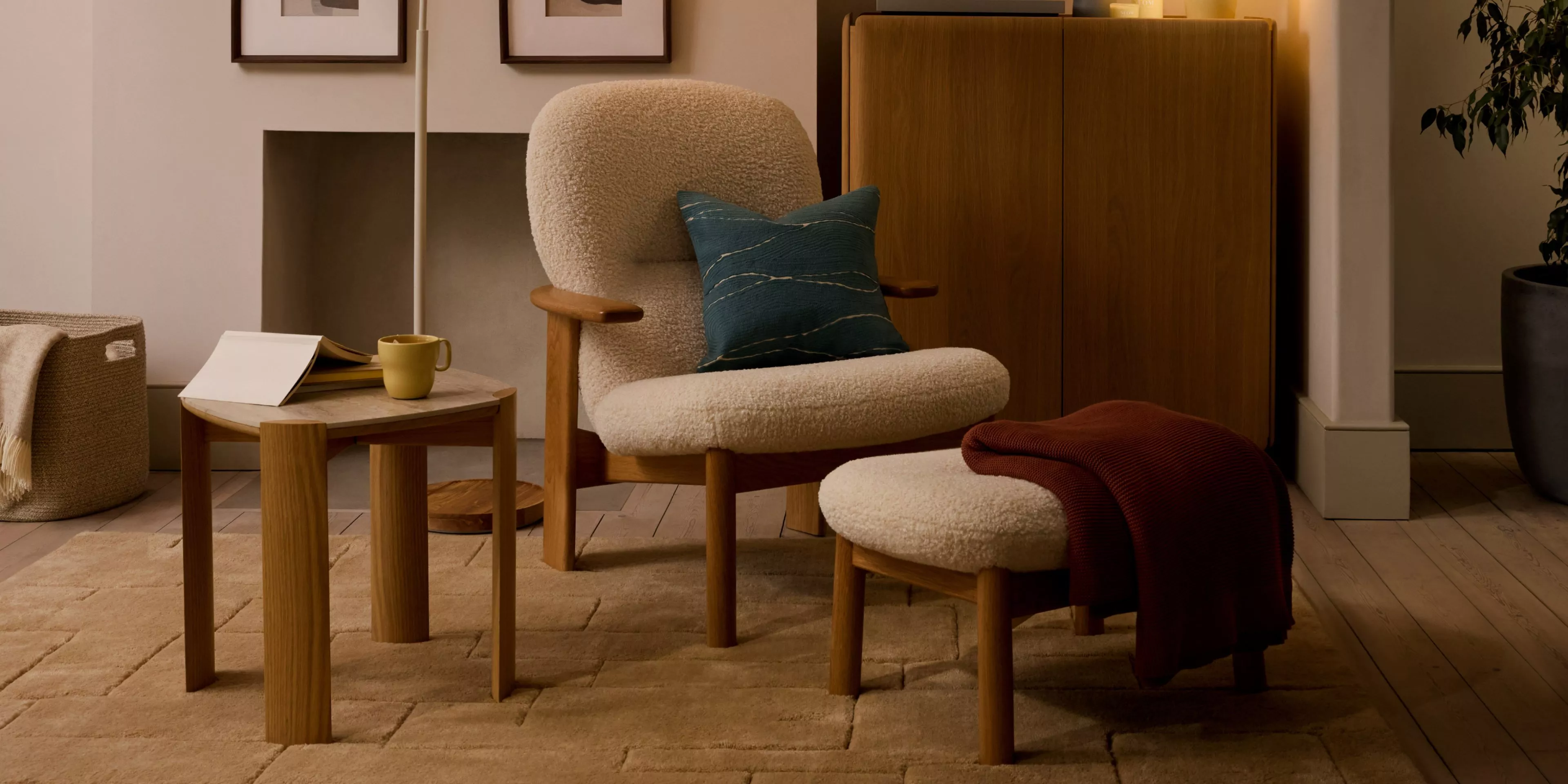 Cosy modern living room with boucle armchair and footstool, wooden side table, cushion and throw blanket