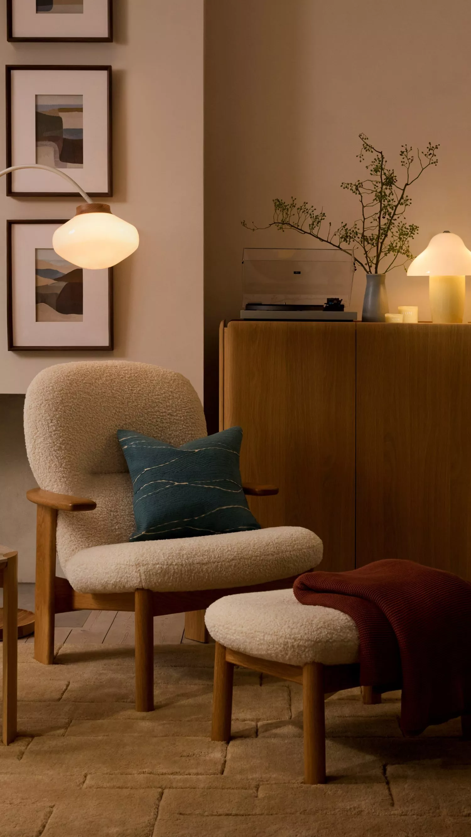 Cosy modern living room with boucle armchair and ottoman, warm lamps, framed art, and wooden sideboard decor