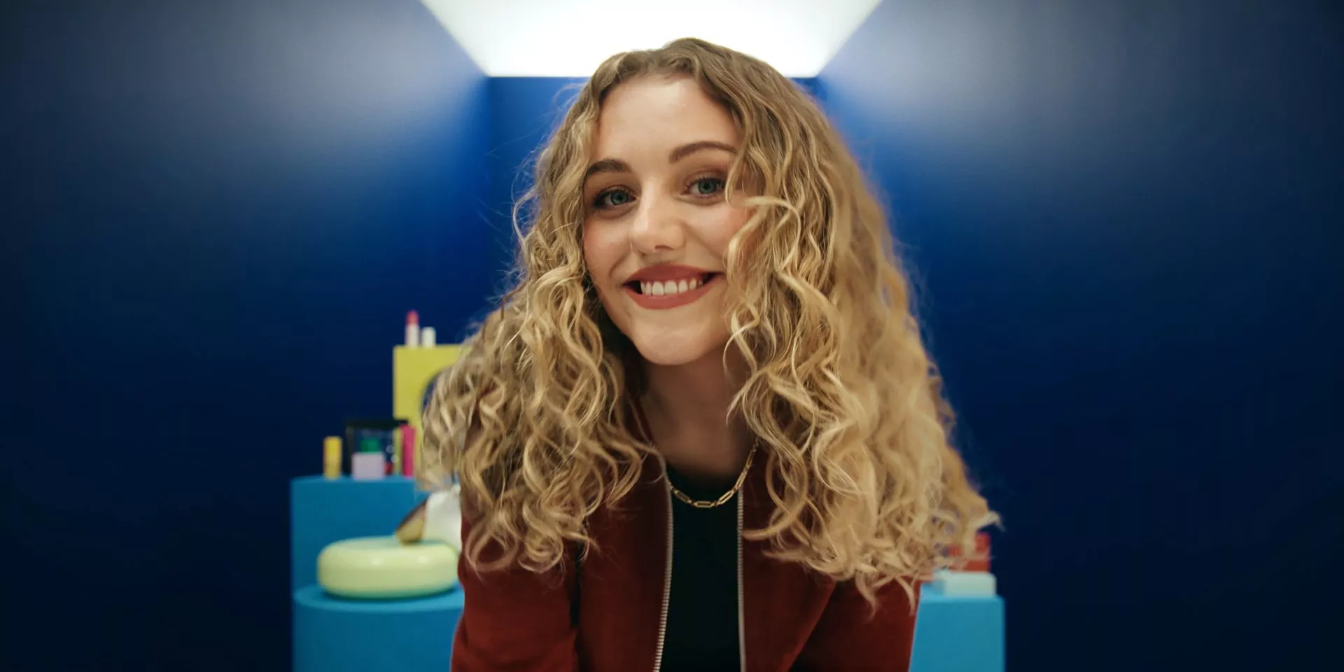 Smiling PR Partner Florence Bretherton with long curly blonde hair in a blue room, modern beauty and lifestyle portrait photo