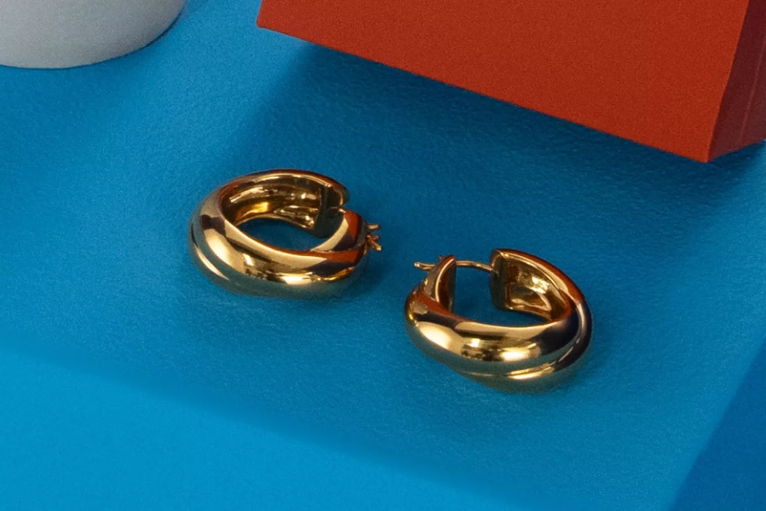 Gold hoop earrings on a blue display, minimal product photography close-up.