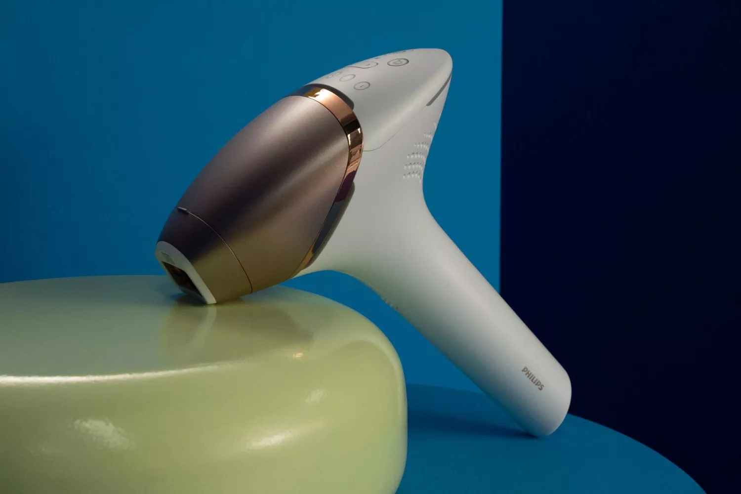 Philips handheld IPL hair removal device resting on a stool, modern home beauty gadget on blue backdrop