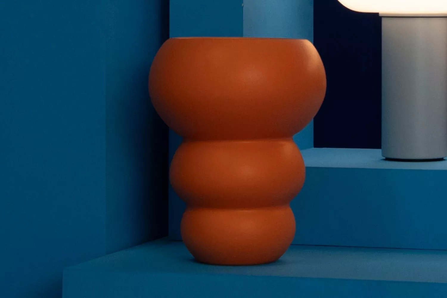 Modern orange sculptural vase on blue platform, contemporary interior design scene