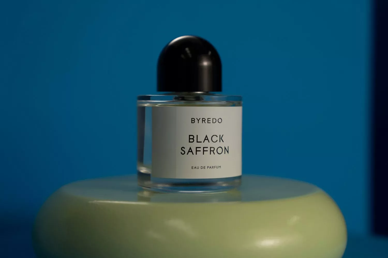 Byredo Black Saffron eau de parfum bottle with black cap on green plinth against blue background