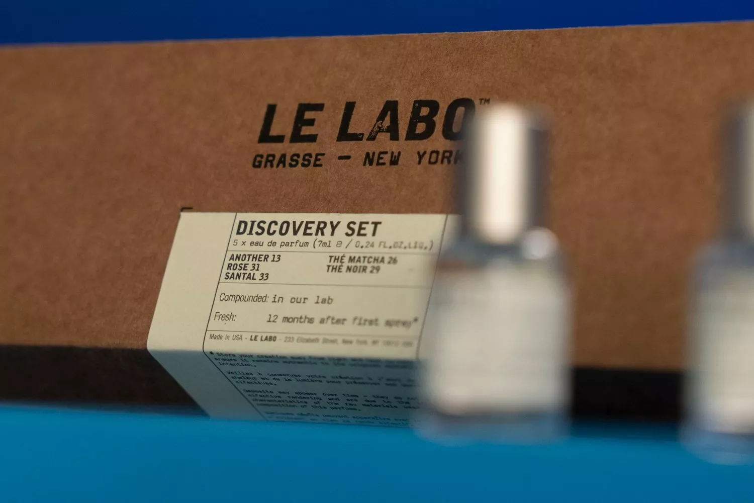 Le Labo Discovery Set perfume box with label, blurred fragrance bottle in foreground on blue background
