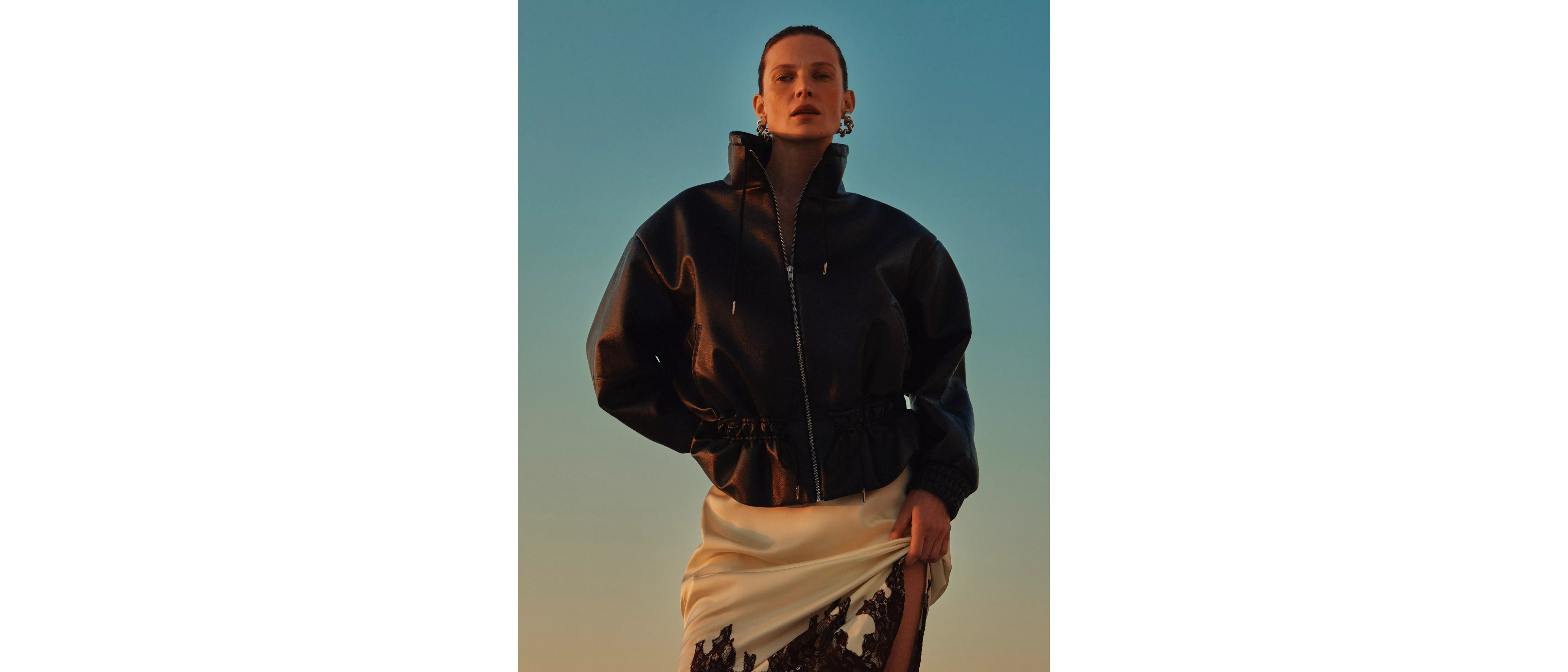 Fashion model in black leather zip-up jacket and beige satin skirt with blue sky background