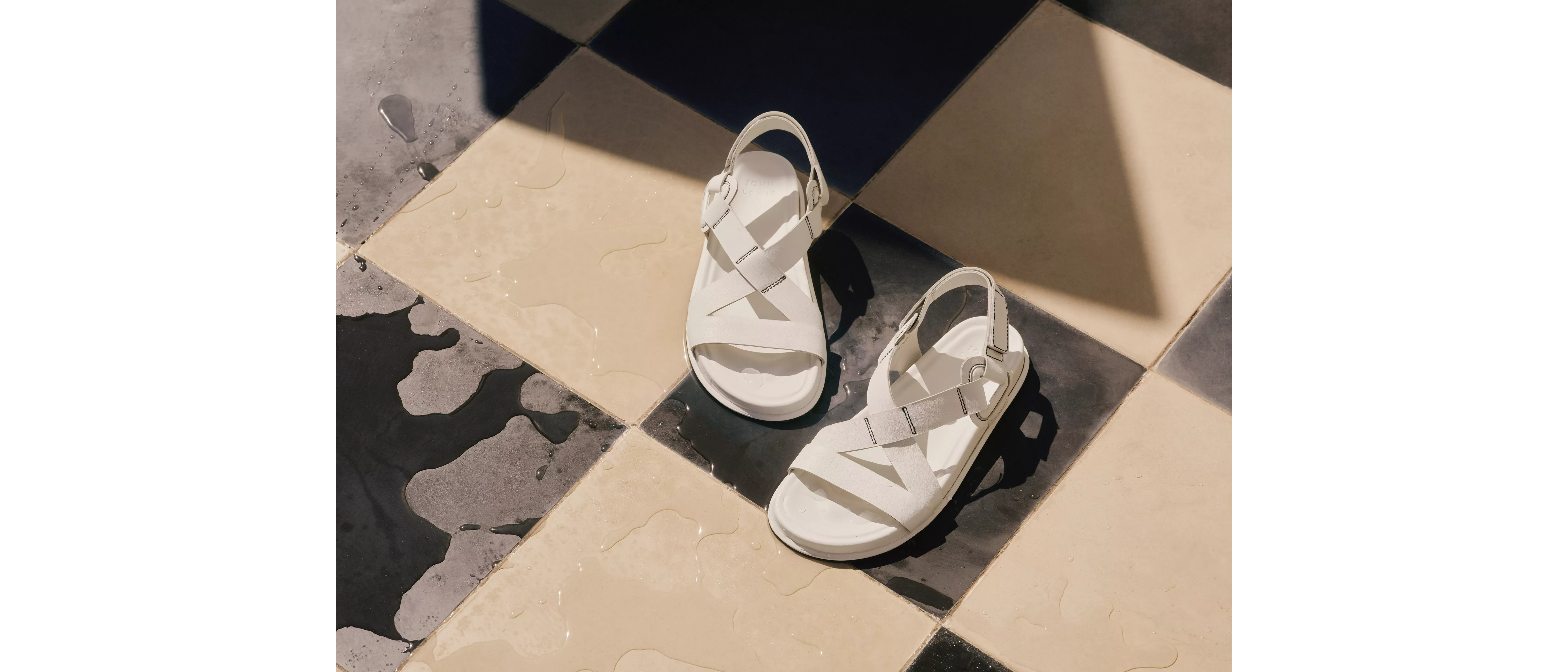 White strappy sandals on wet beige and black tiled floor and sunlit shadows