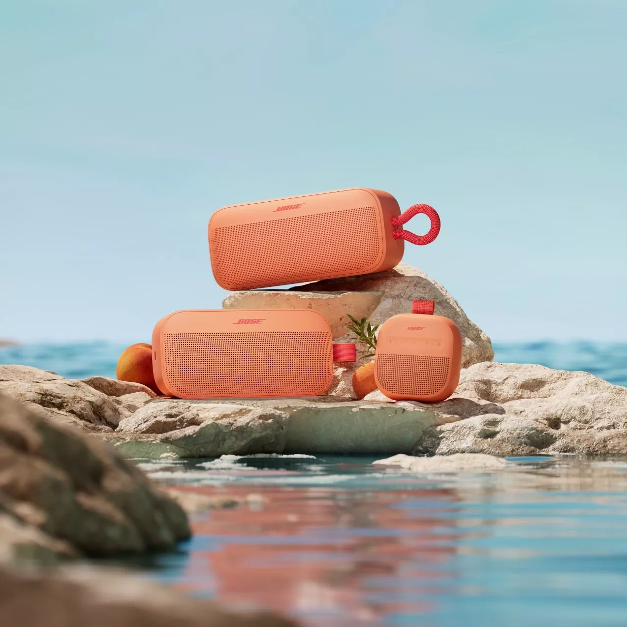 Orange Bose portable Bluetooth speakers on seaside rocks, waterproof outdoor audio with ocean backdrop