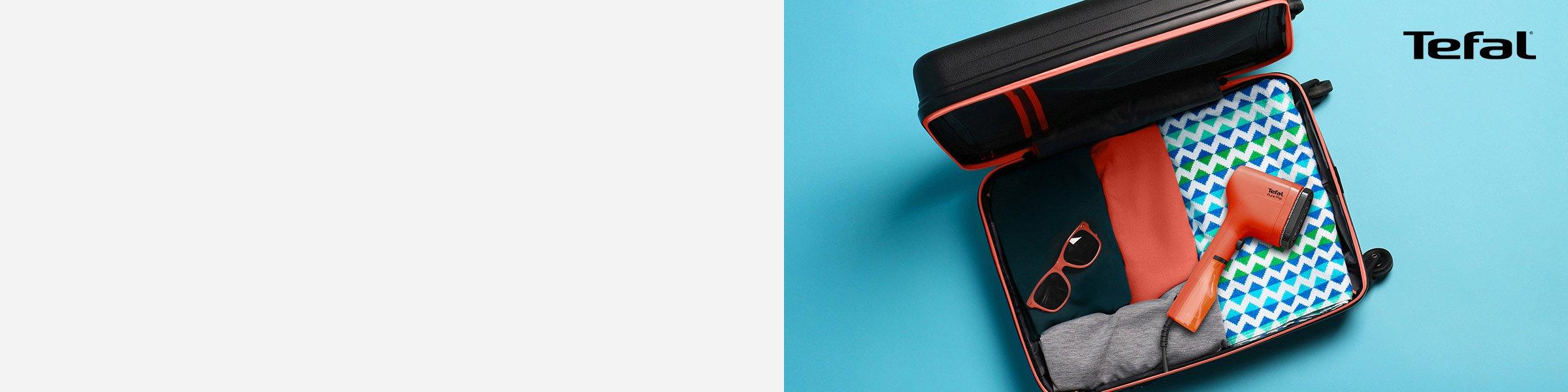 Orange Tefal garment steamer placed on folded clothes in a suitcase.