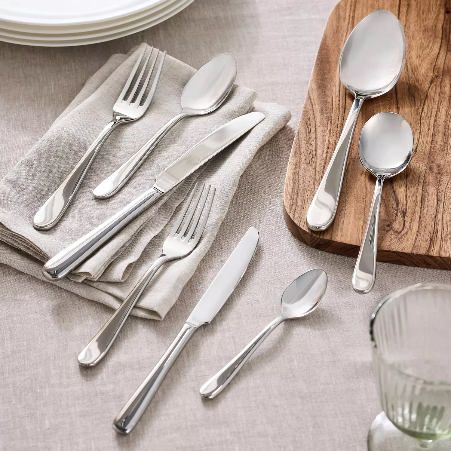Shine silver cutlery laid out on a table with plates, napkins and a glass