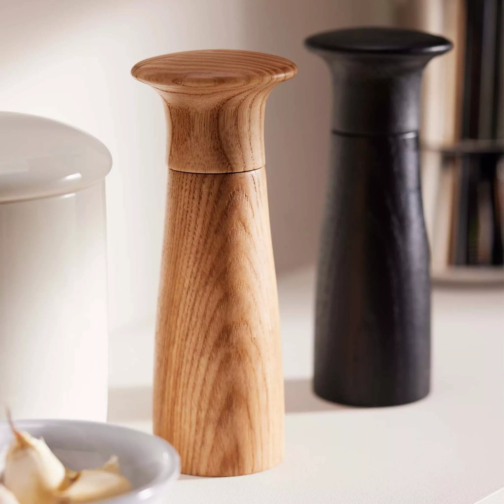 Close-up of wooden and black salt and pepper mills on a kitchen worktop with ceramic jar and garlic bowl
