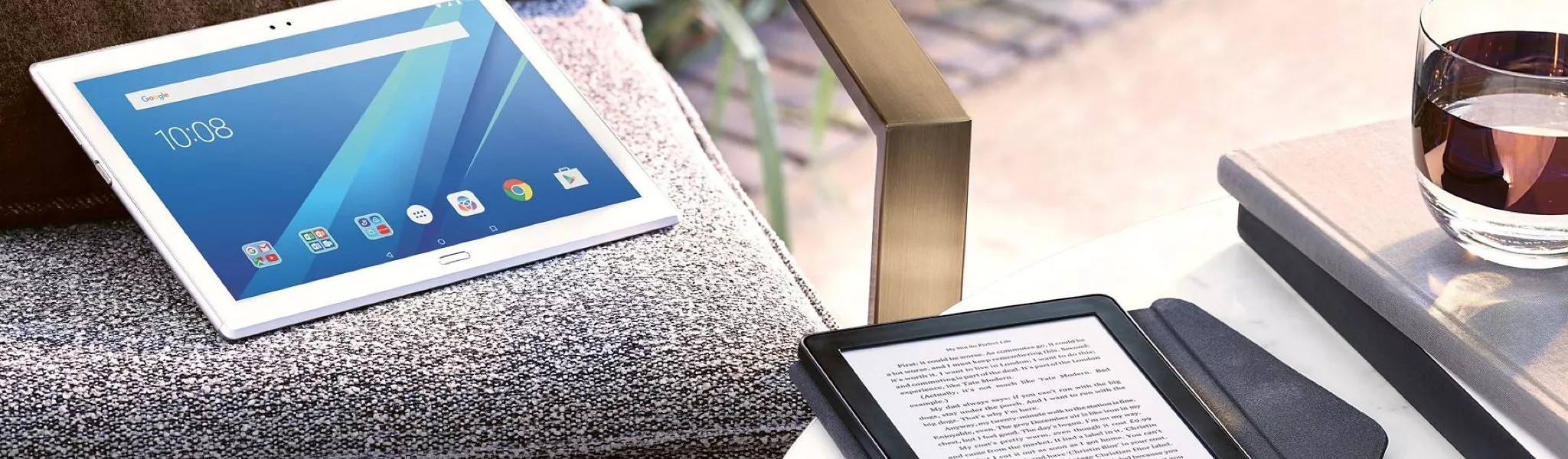 Tablet and e-reader on outdoor sofa with coffee on table, modern digital reading and browsing setup
