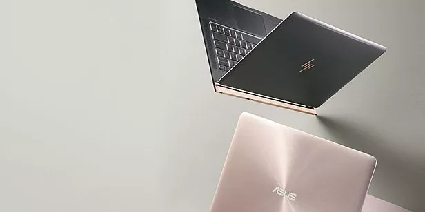 Two slim laptops on a grey desk, one open showing keyboard, modern business notebook computer setup view
