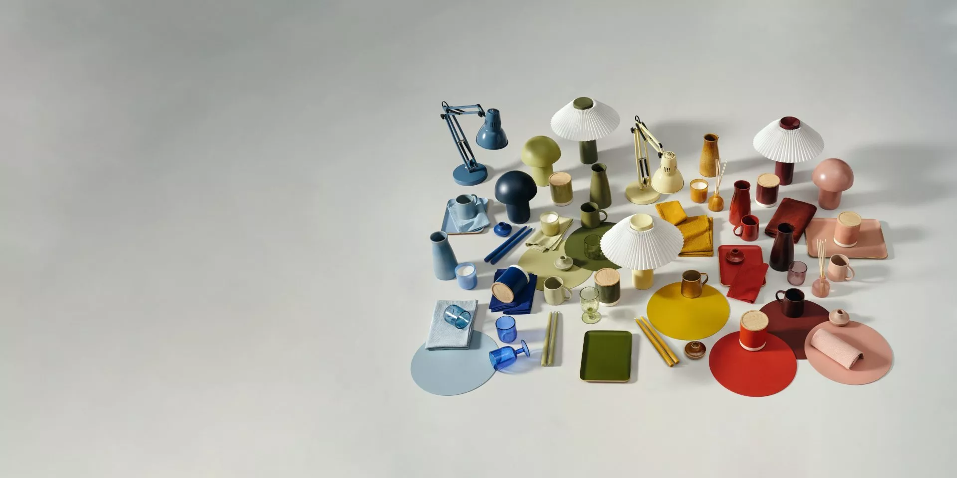 Colourful modern tabletop still life with lamps, mugs, vases and trays arranged on a grey studio background