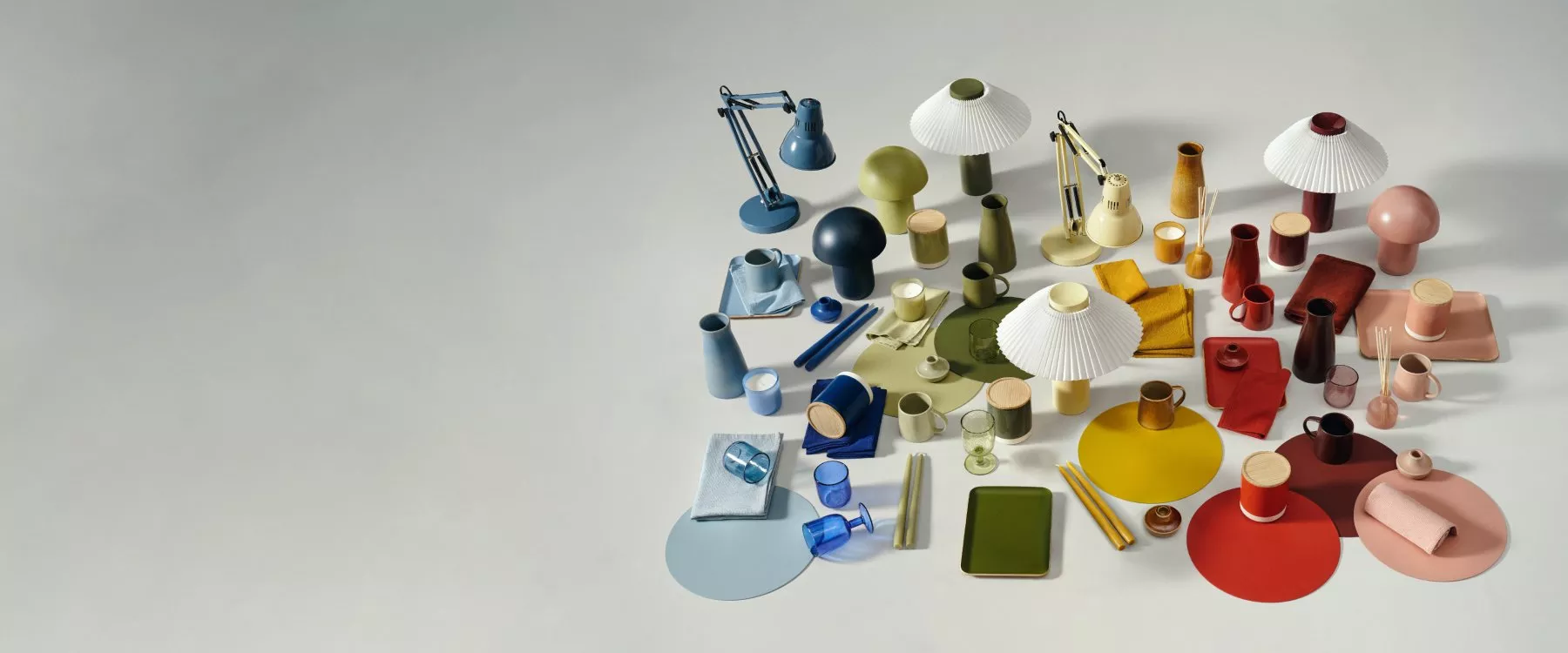 Colourful modern homeware flat lay with table lamps, mugs, vases, trays and textiles on a neutral background
