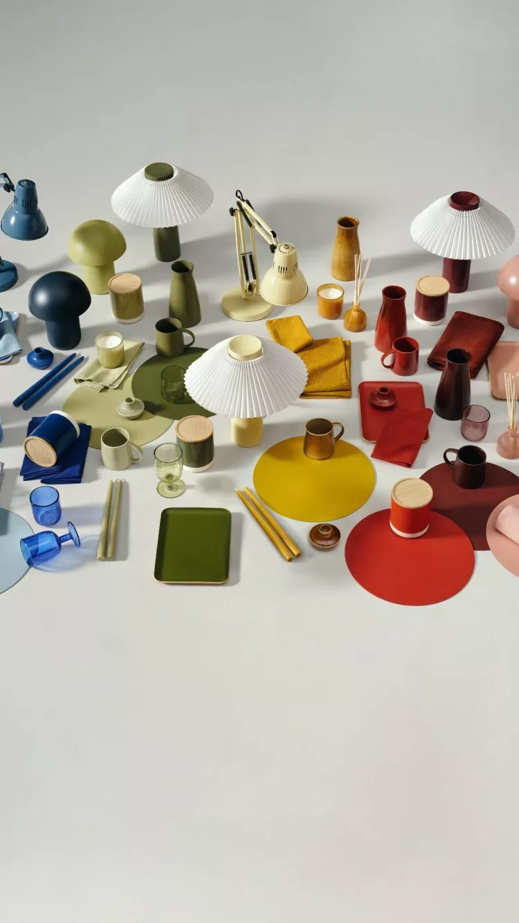 Colourful modern tableware and lamps arranged on a white backdrop, featuring mugs, plates, vases and placemats