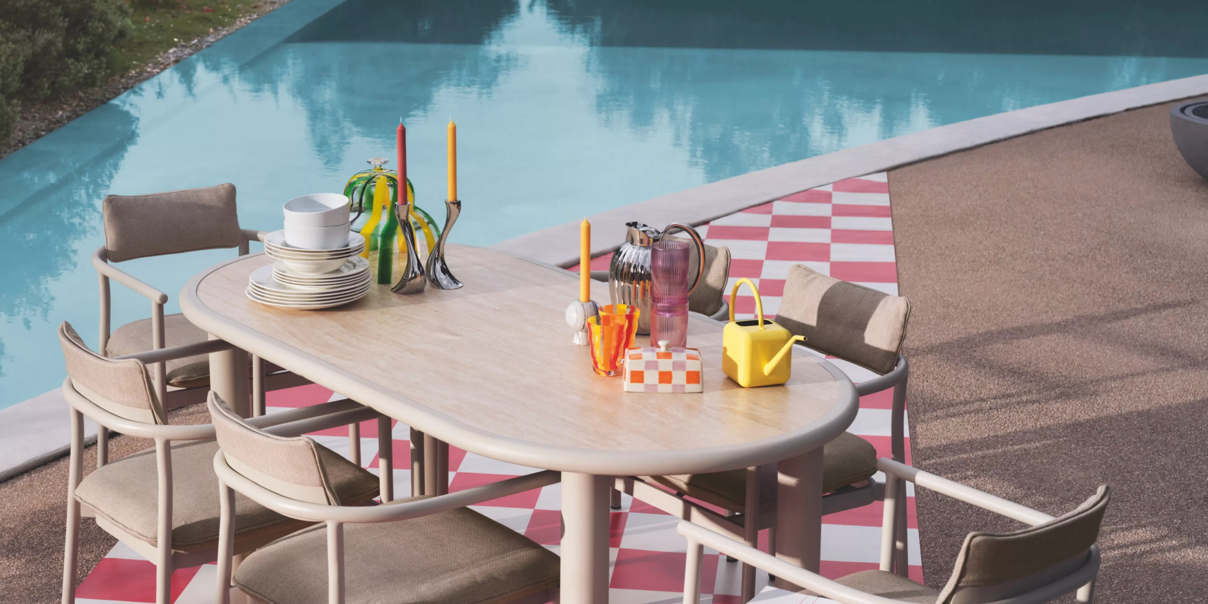 Poolside dining setup with colourful  tableware and modern furniture on a chequered patio.