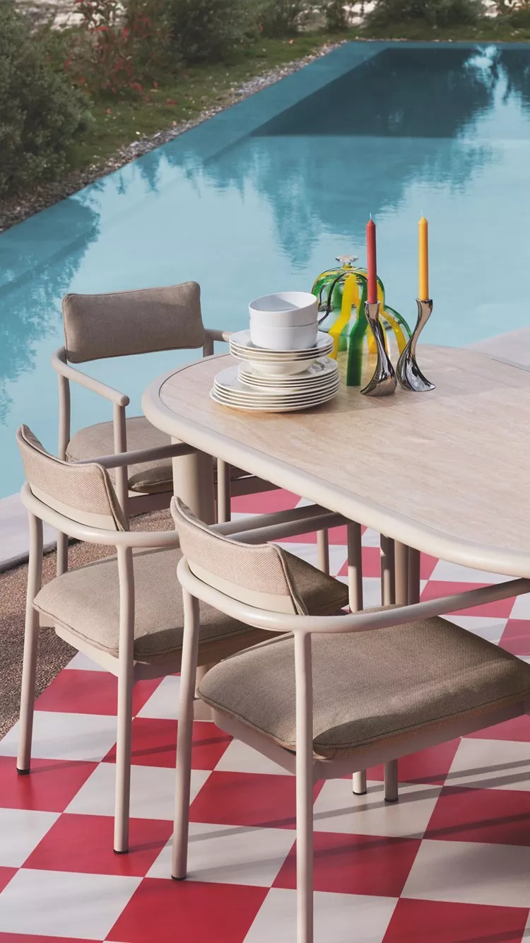 Poolside dining setup with colourful  tableware and modern furniture on a chequered patio.