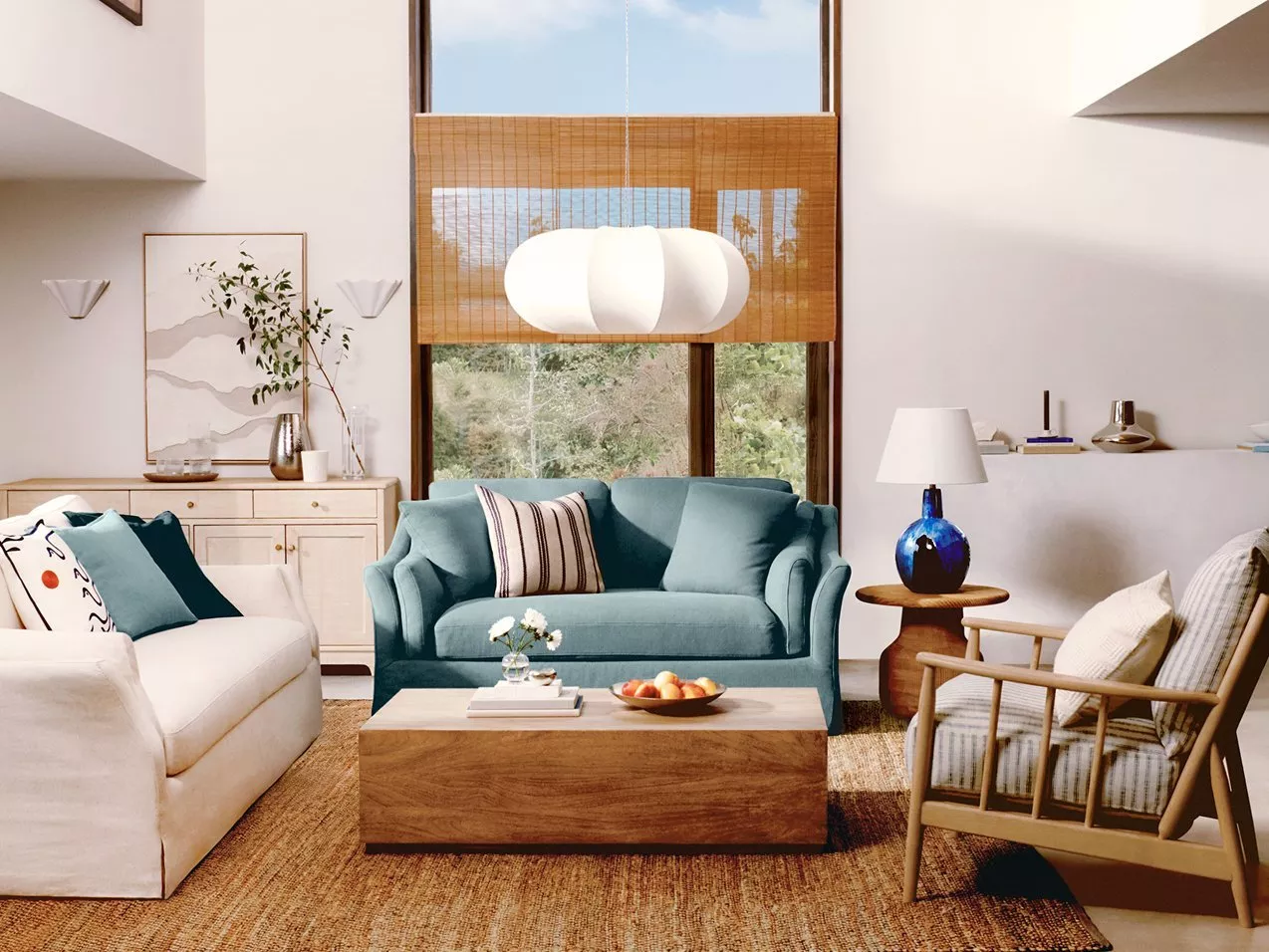 Modern living room with teal sofa, wooden coffee table, woven rug and large window with bamboo blind