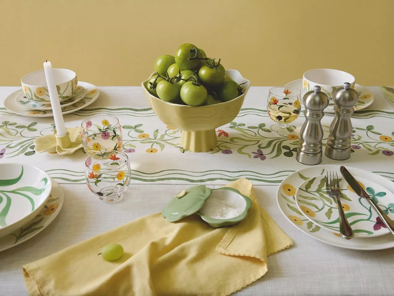Stylish dining table set with floral crockery, green tomatoes centrepiece, glassware and salt and pepper mills