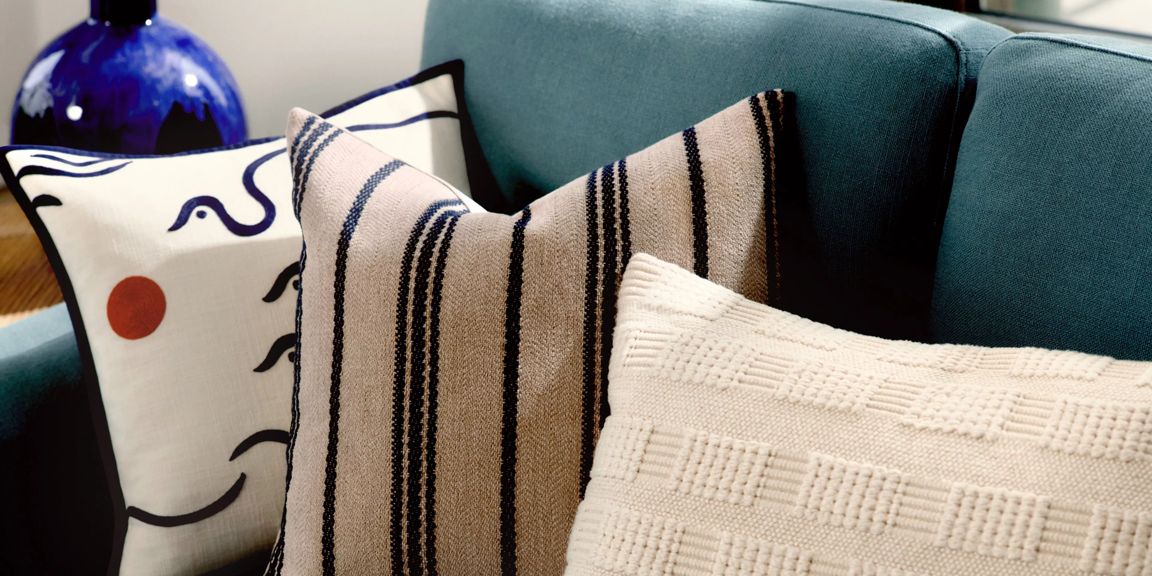 Living room with teal and off white sofa, wooden coffee table, and hanging ceiling light with sculptural lampshade.
