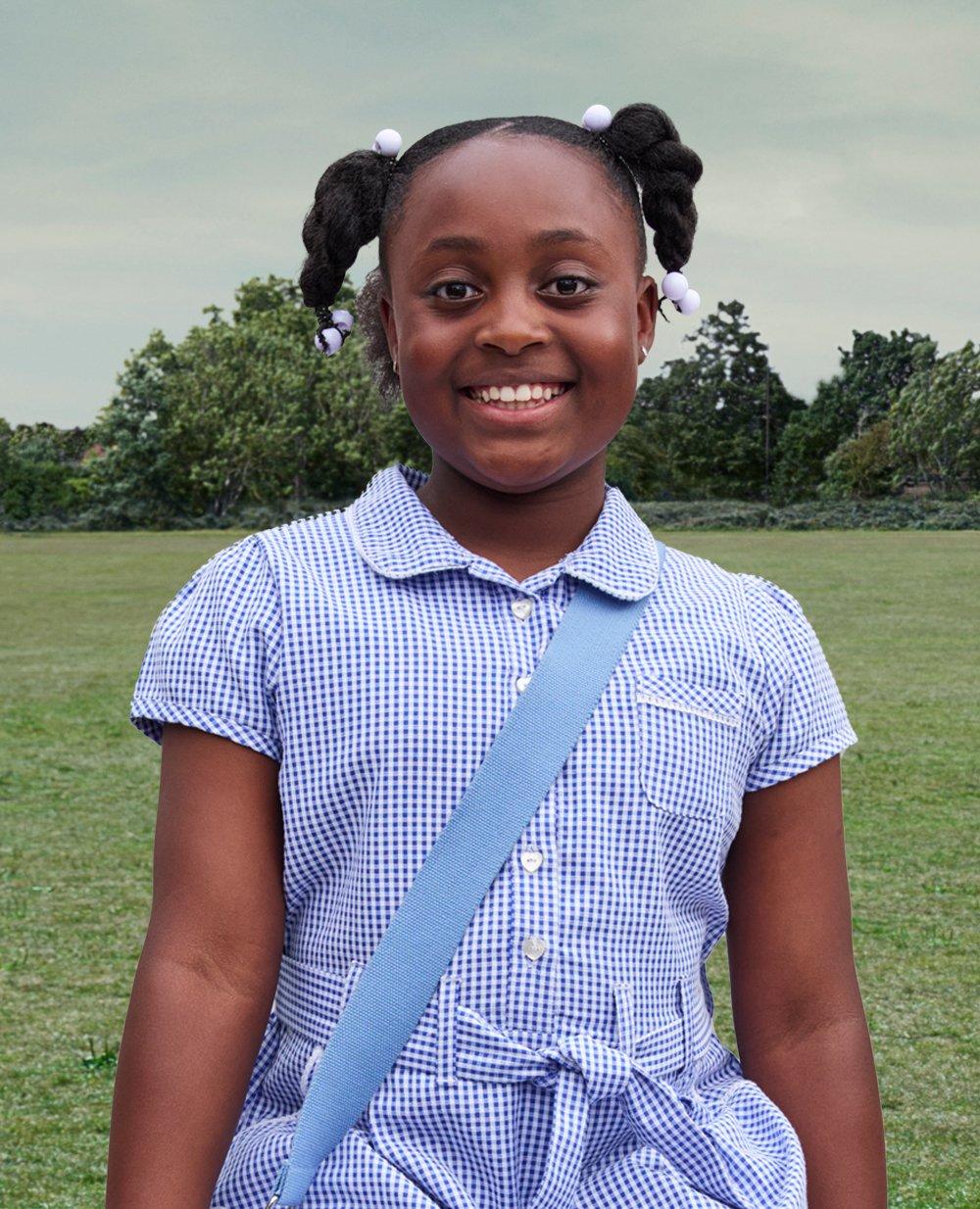 a kid standing in a field wearing her school uniform