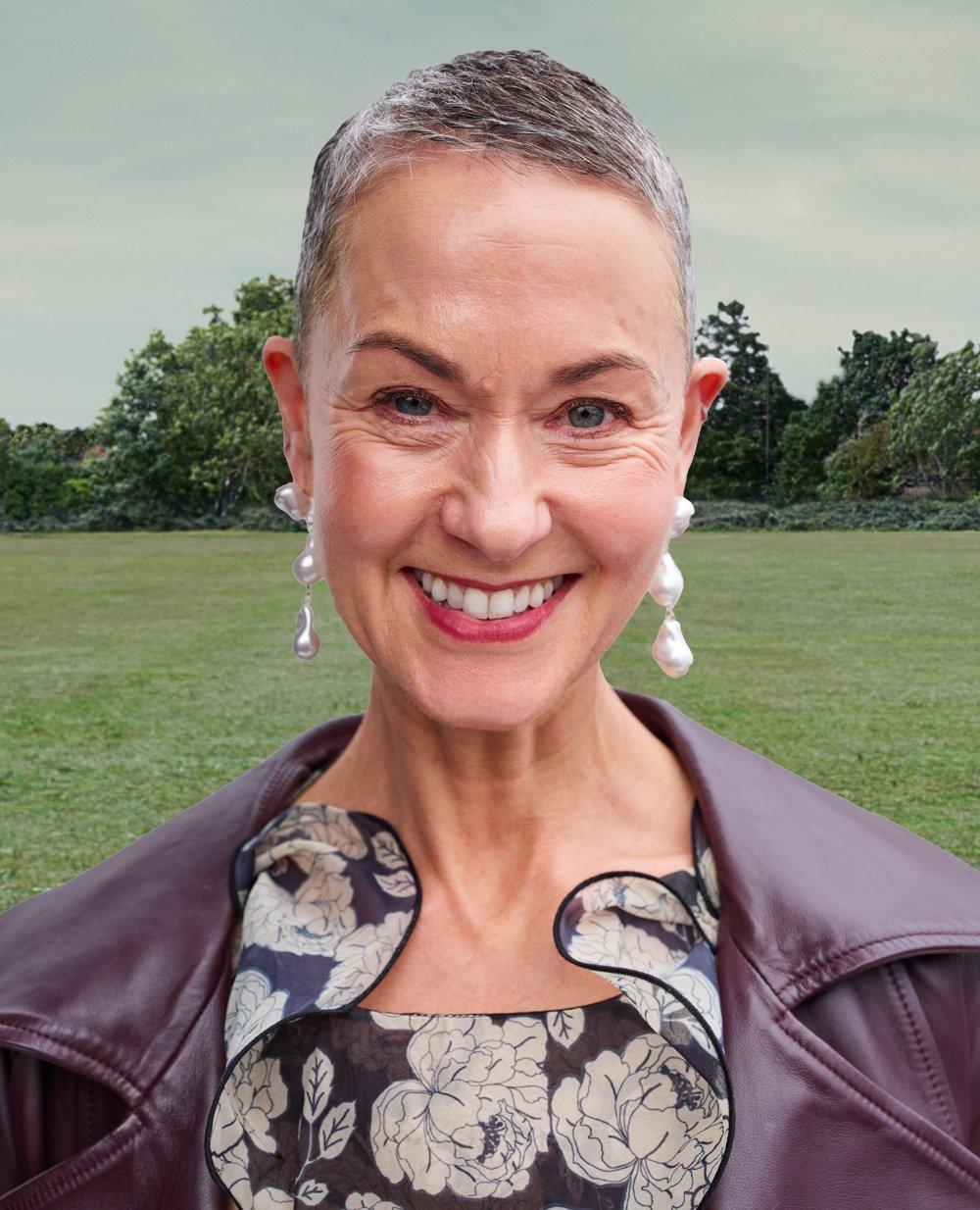 a woman facing the camera smily wearing a purple leather jacket standing in a field