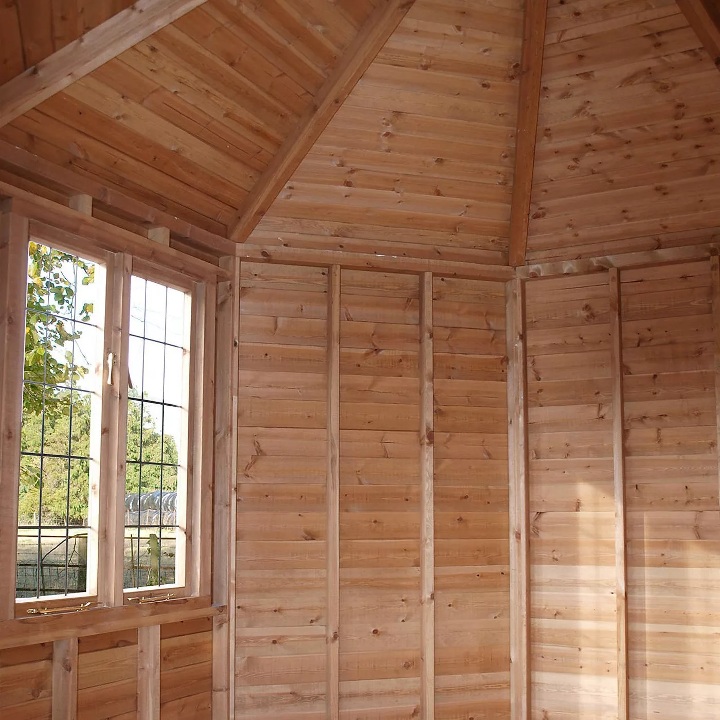Interior of a wooden garden summerhouse with pitched roof, timber wall framing and leaded window view