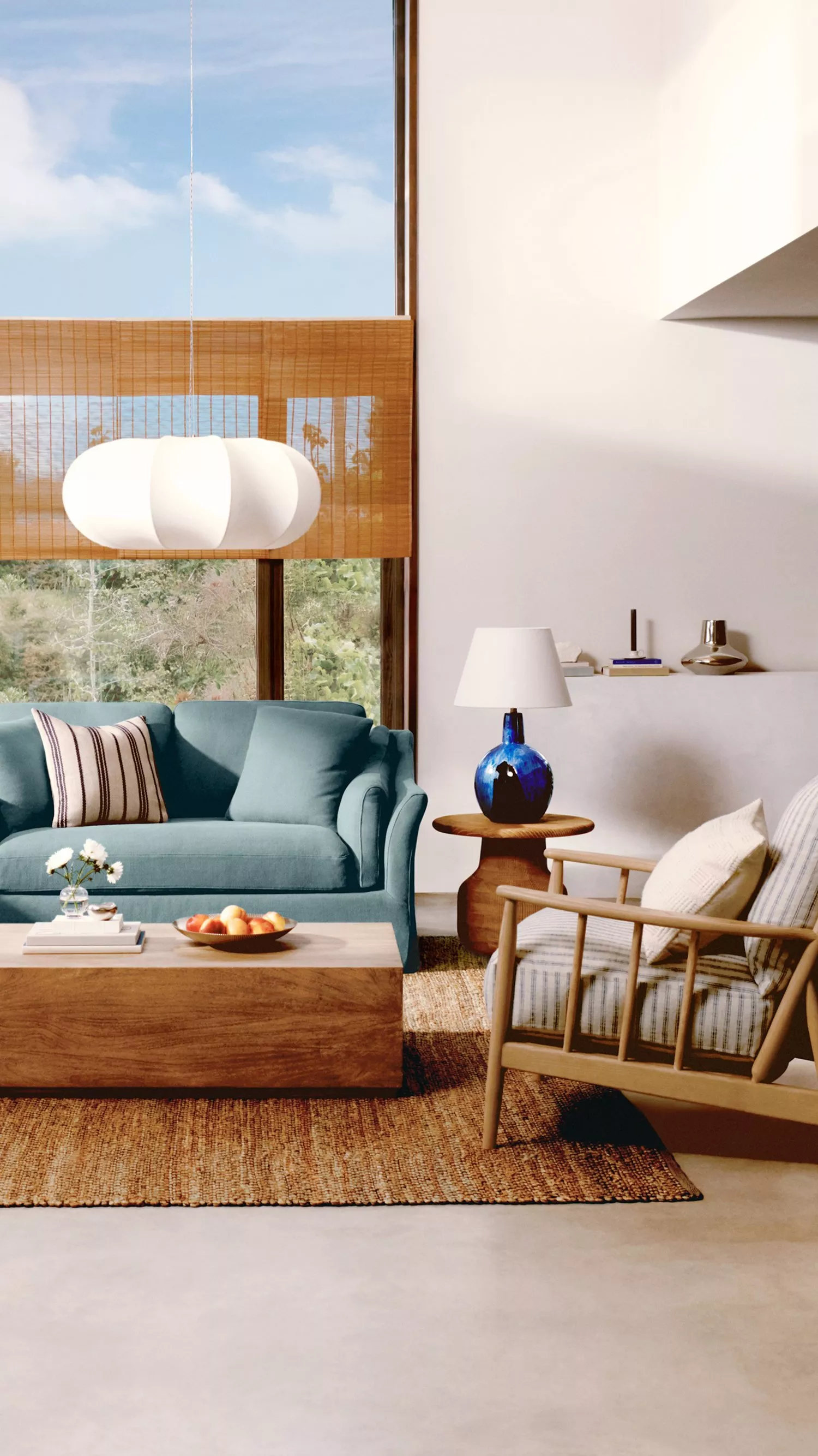 Modern living room with a teal sofa, wooden furniture, and a large window with a scenic view. Cosy and stylish decor.