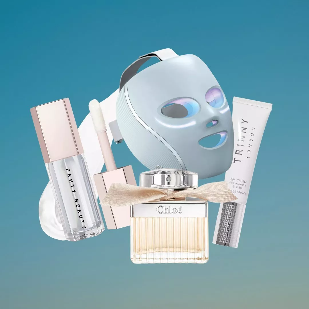 Beauty flat lay with LED face mask, Fenty Beauty lip gloss, Chloé perfume and Trinny London cream on blue background