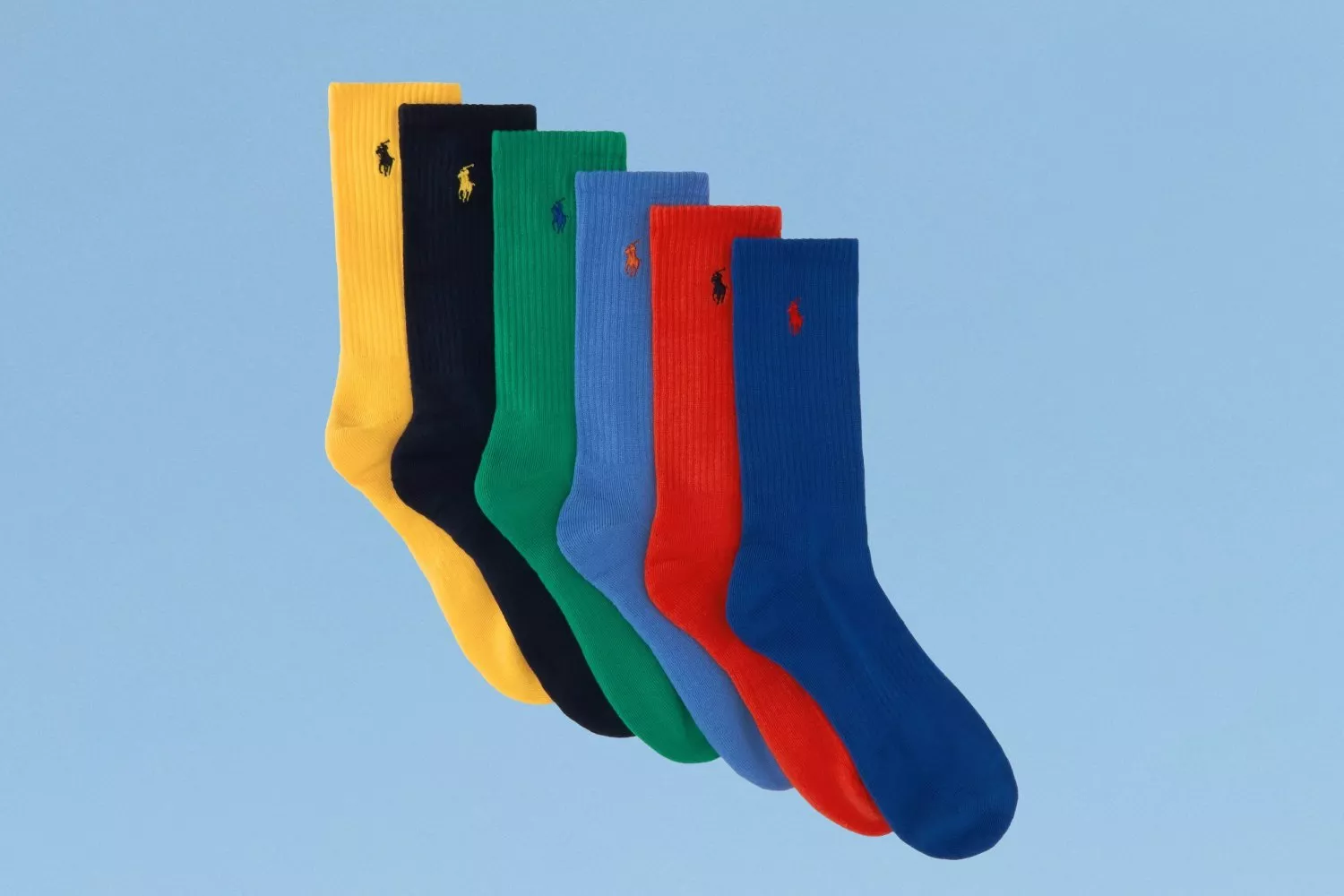 Five colourful ribbed crew socks in yellow, navy, green, light blue and red on a pale blue background