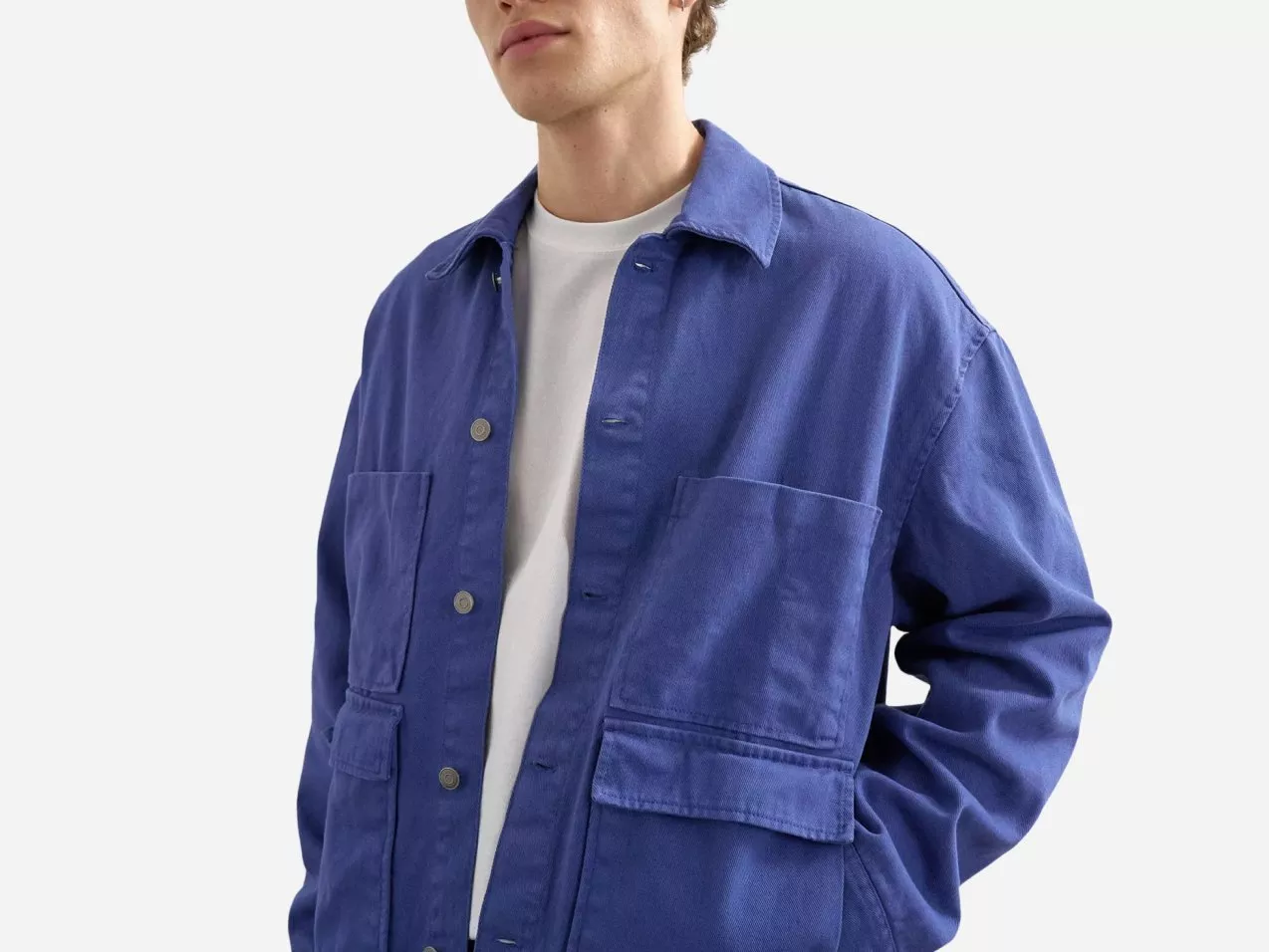 Men’s blue cotton chore jacket with button front and patch pockets, styled over a white T-shirt on model