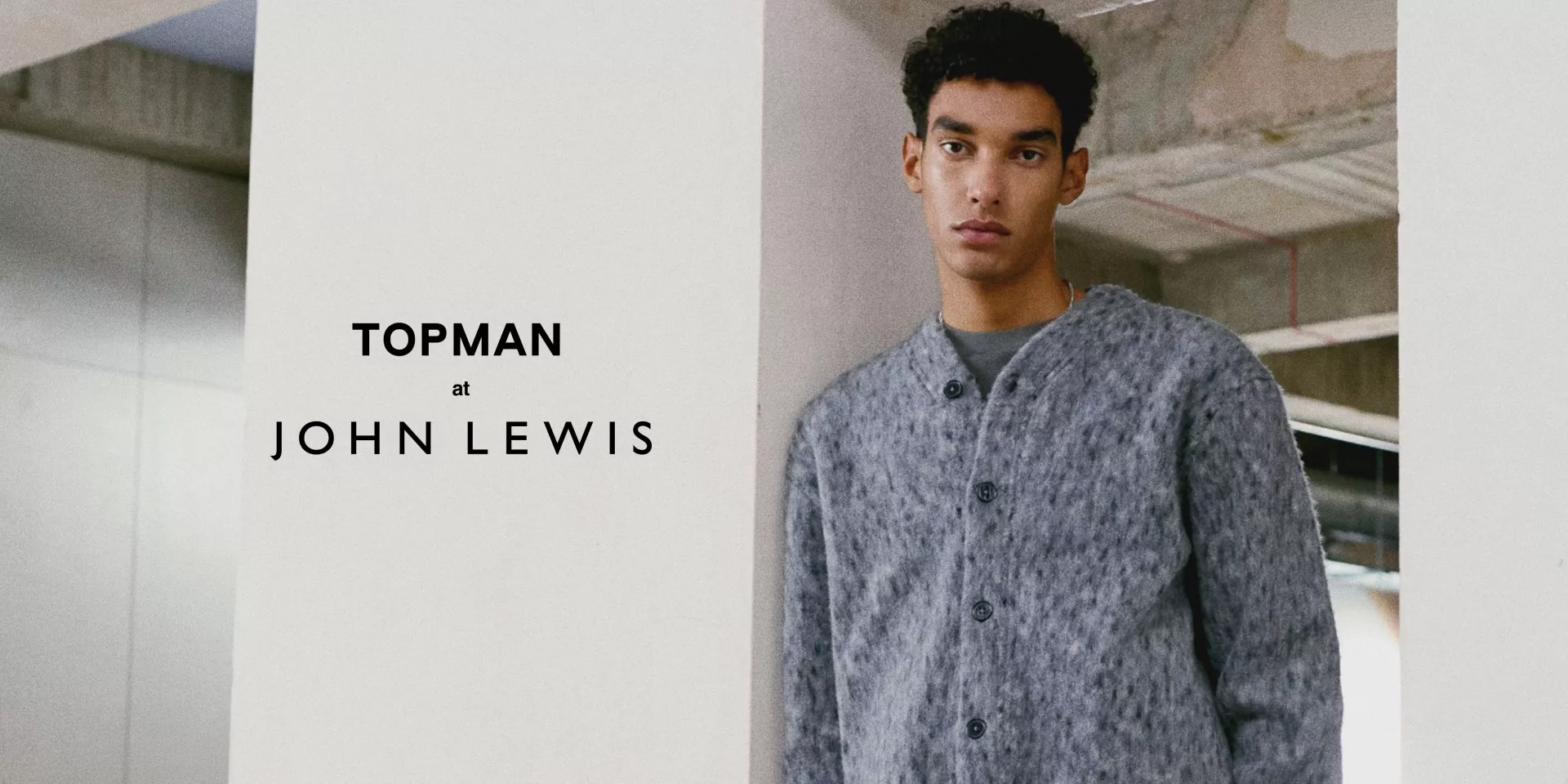 Topman at John Lewis menswear campaign with model wearing grey button cardigan in a modern concrete interior.