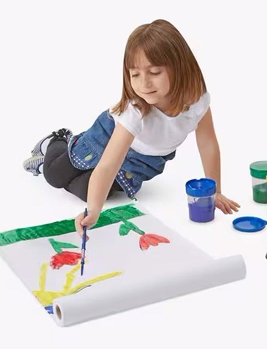 A child painting on a large sheet of paper with various art supplies around her.