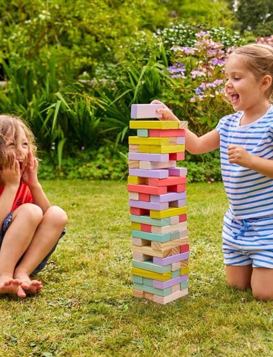 The image shows two children playing a game with colorful wooden blocks in an outdoor setting, likely in a garden