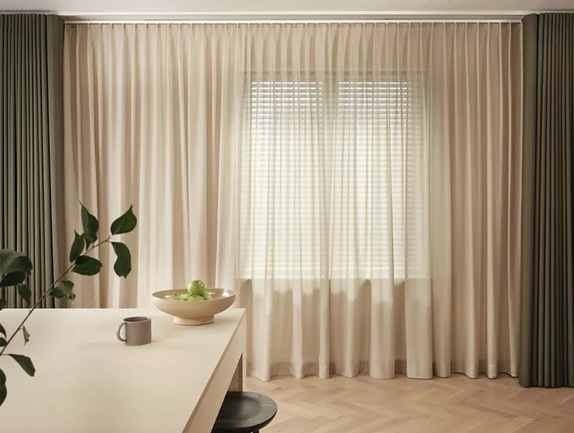 Stylish interior with sheer beige curtains, green drapes, and a minimalist table featuring a plant and bowl.