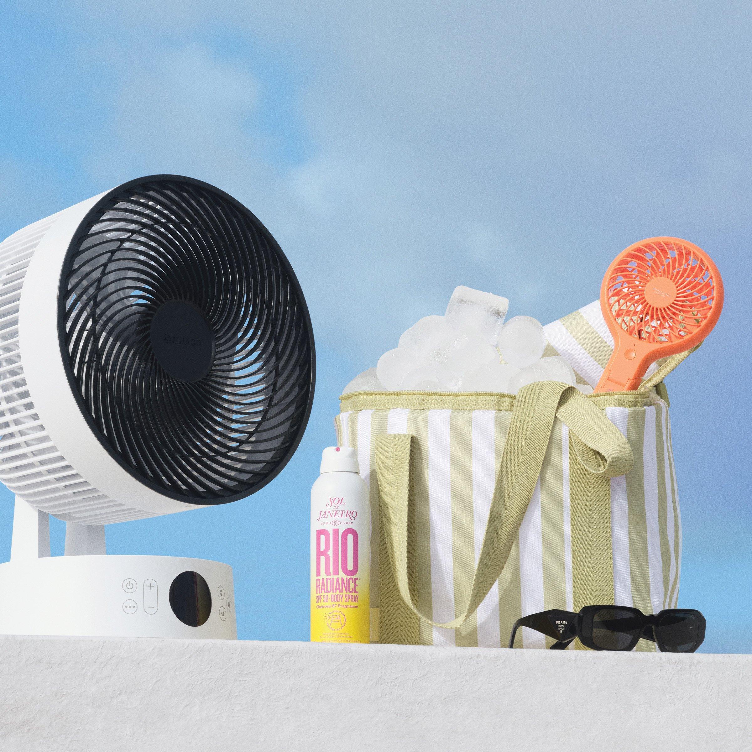 Large standing electric fan, with smaller hand fan in inside beach bag. Sol de Janeiro SPF spray and sunglasses in front of beachbag.
