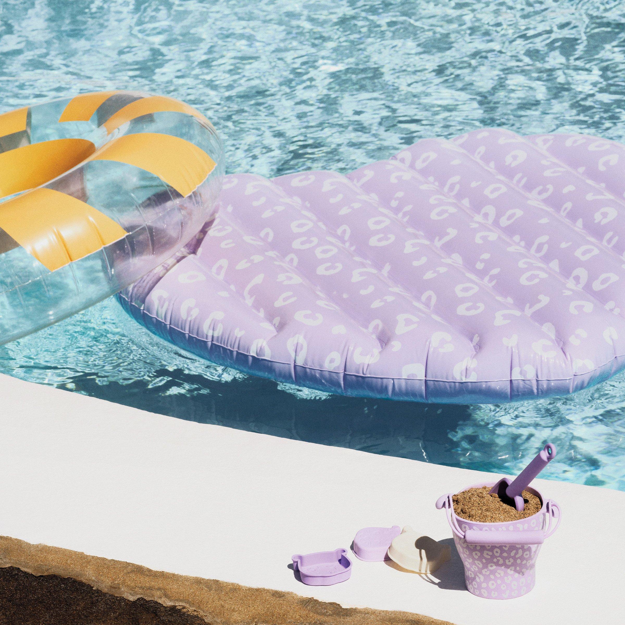 Stripey inflatable pool ring and float, floating in pool, with kid's bucket of sand and spade on pool side.