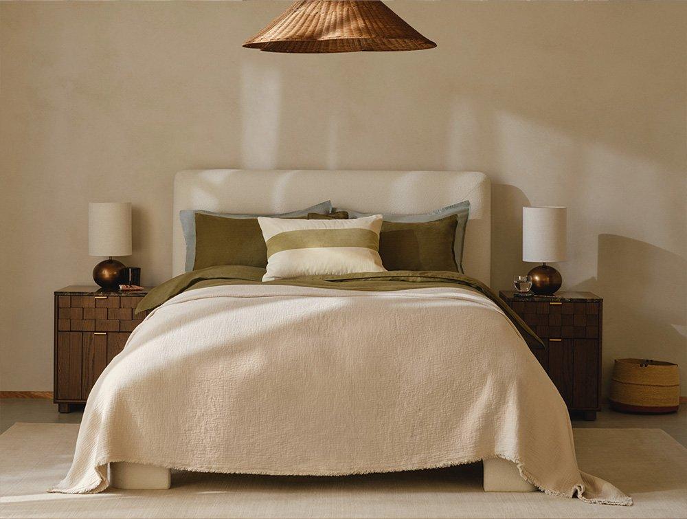 Double bed with white bedspread and dark green cushions, and side tables either side.