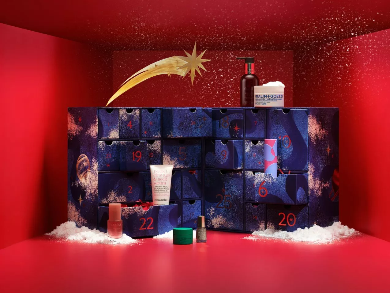 Beauty advent calendar with numbered drawers, skincare minis and festive red background with snowflakes and shooting star.
