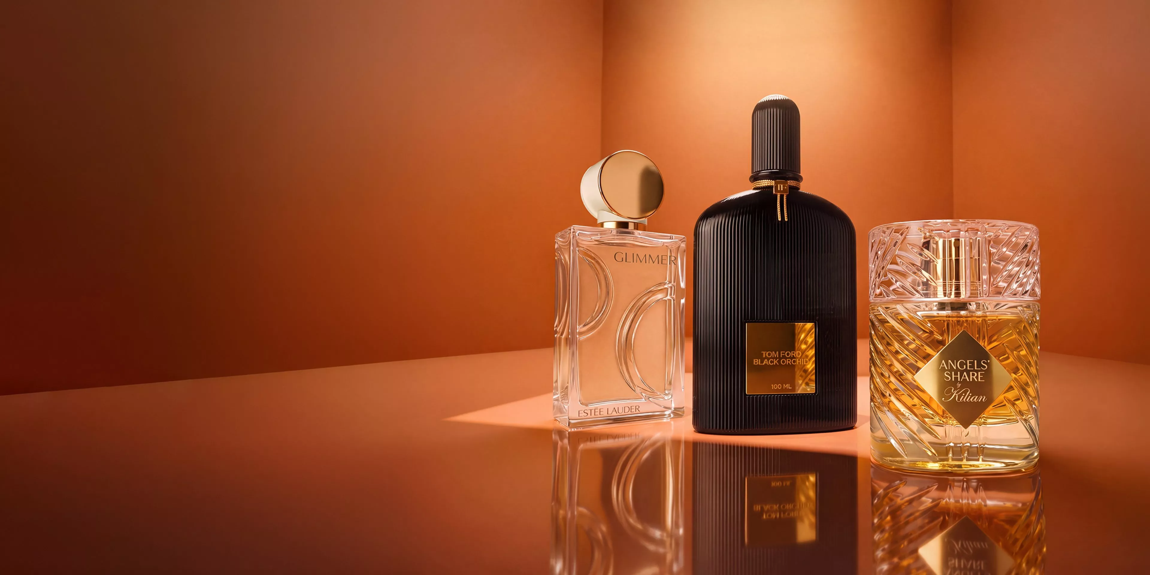 Luxury perfume bottles on warm orange background, featuring designer fragrances in reflective studio lighting