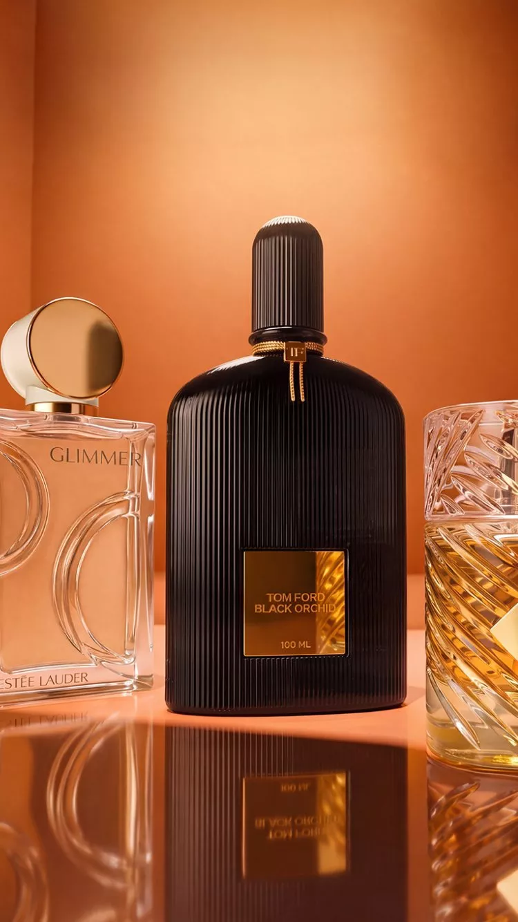 Tom Ford Black Orchid perfume bottle with other luxury fragrances on a warm orange studio background, close-up.