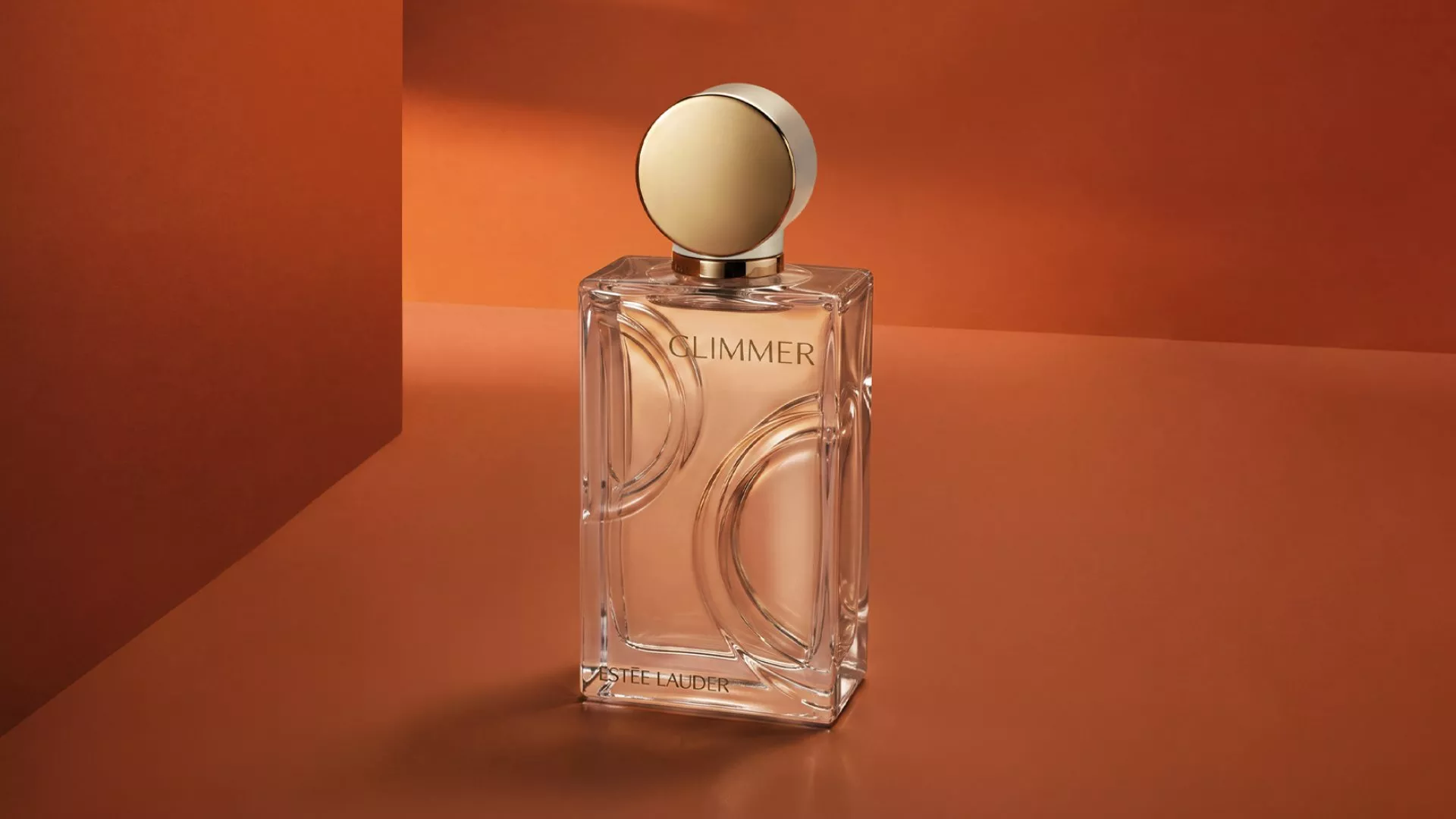Estée Lauder Glimmer perfume bottle with gold cap on warm orange background, luxury fragrance product shot