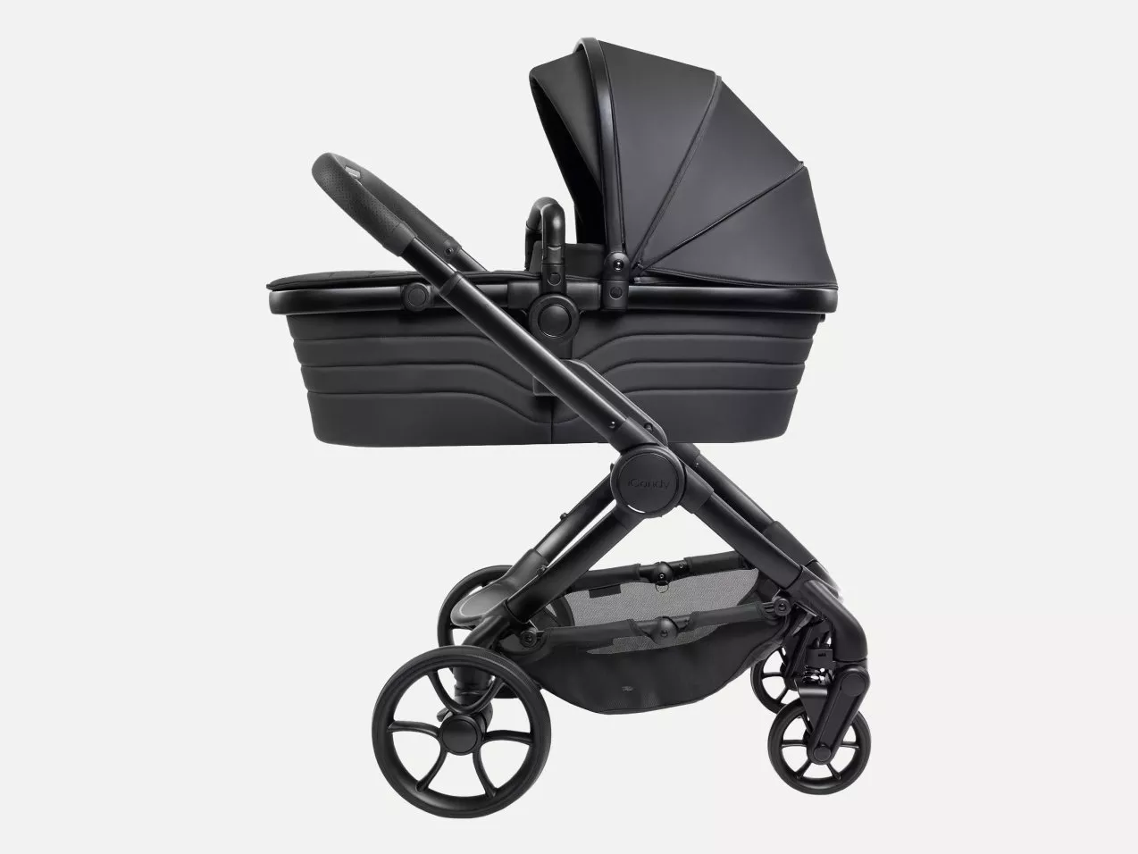 Black baby pram carrycot on pushchair chassis, side view with large wheels and extended canopy on white background