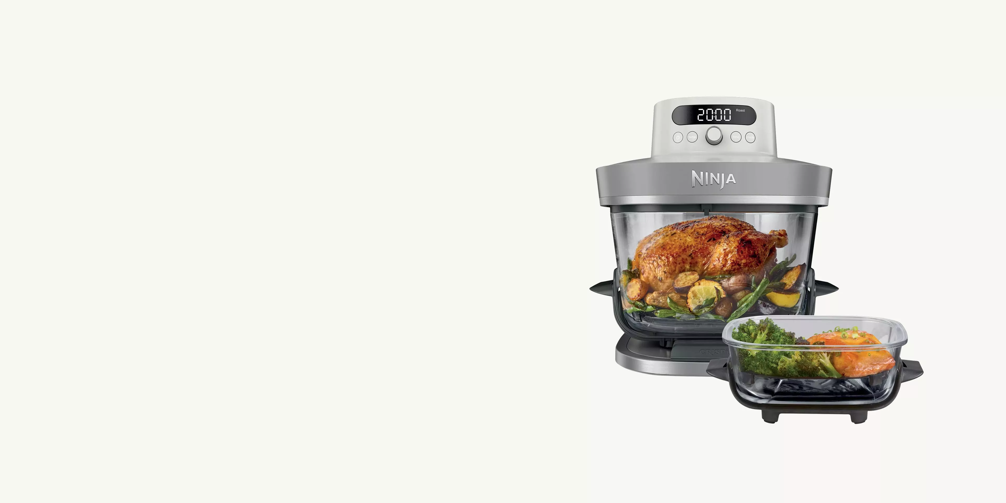 Ninja air fryer oven with glass bowl roasting whole chicken and vegetables, plus tray with salmon and greens