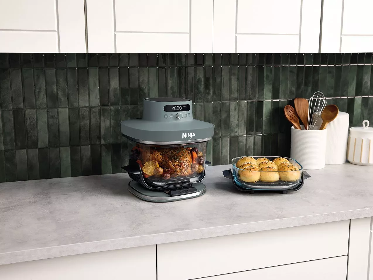 Ninja air fryer and multicooker on kitchen worktop, roasting whole chicken with tray of baked bread rolls
