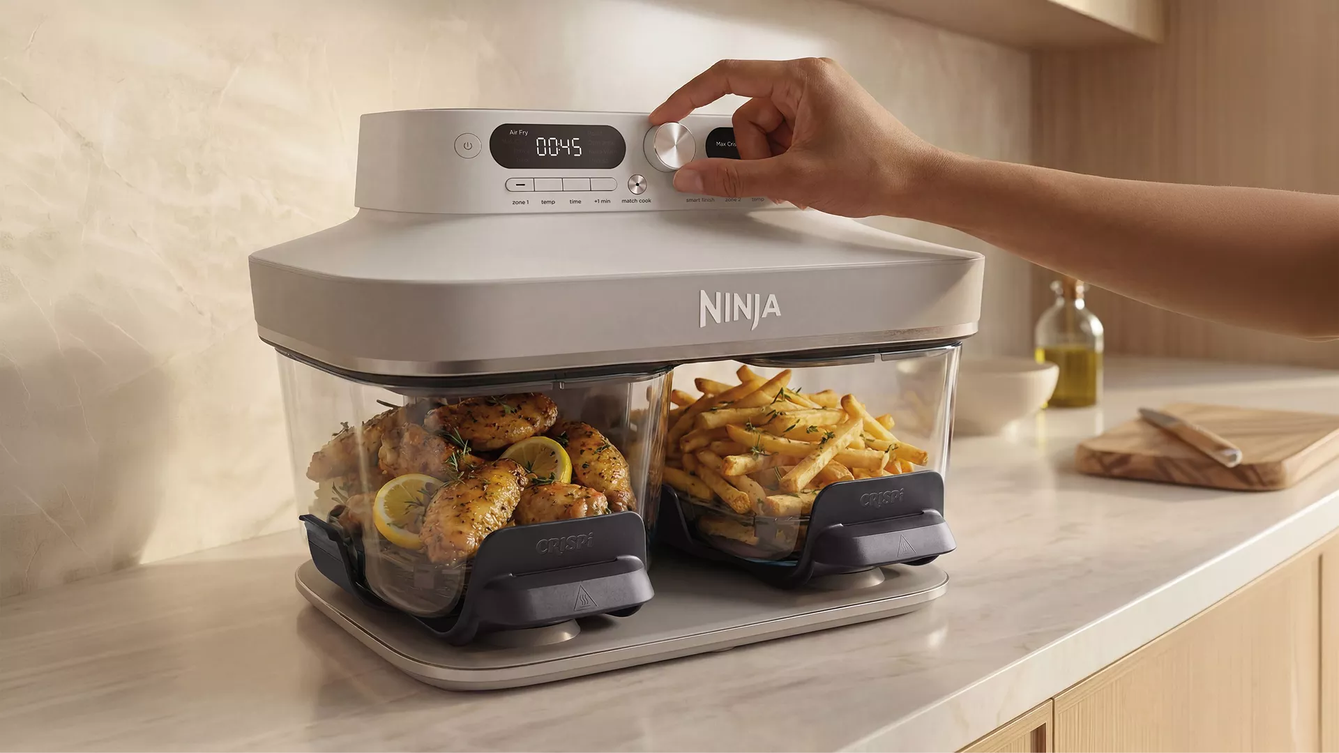 Ninja dual zone air fryer with chicken and chips, hand adjusting dial on kitchen worktop for fast cooking