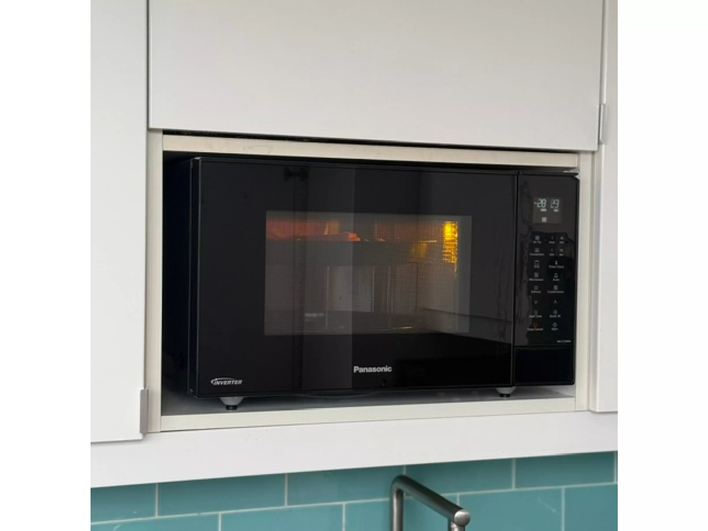 Black Panasonic microwave oven built into white kitchen cupboard, digital controls visible, modern cooking appliance close-up