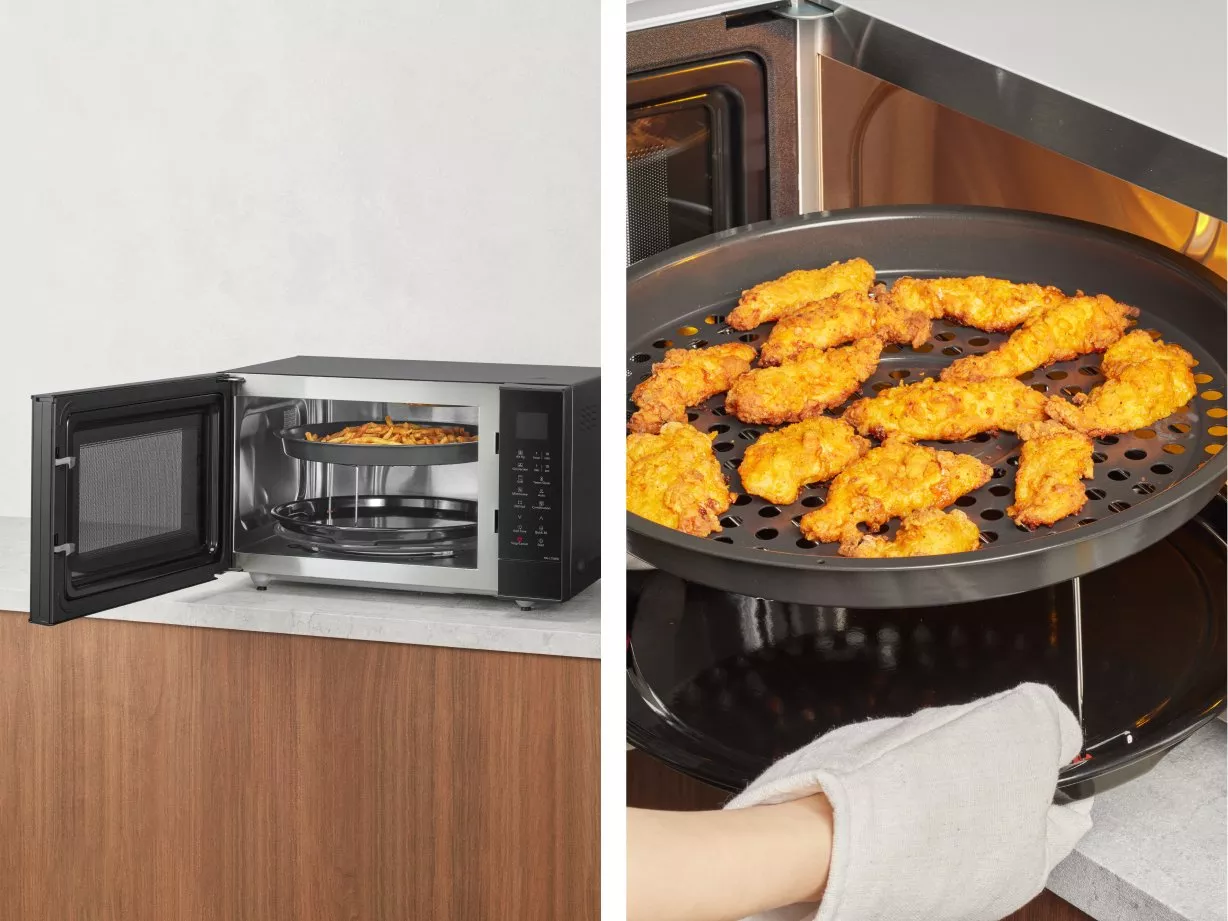 Open microwave oven with air fryer tray cooking crispy chicken wings on a kitchen worktop, close-up detail